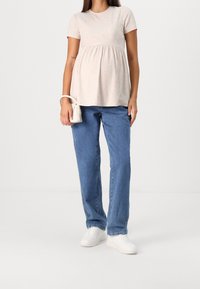 Ljus beige kortärmad topp med ribbad textur, lös passform och samlad midja, tillsammans med blå rakbenade jeans och vita sneakers.