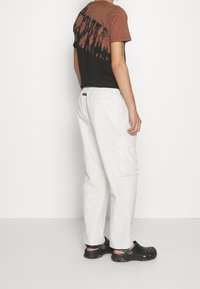 Brown and black tie-dye t-shirt with short sleeves, paired with white cargo pants featuring side pockets, and black clogs. Simple design.