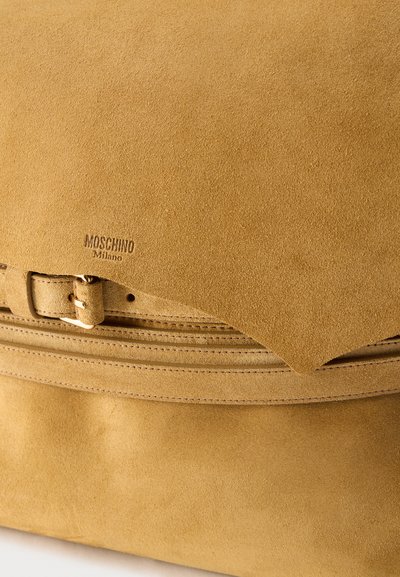 Sac à main en daim couleur tan avec un détail ceinture et "Moschino Milano" embossé sur la partie avant supérieure.