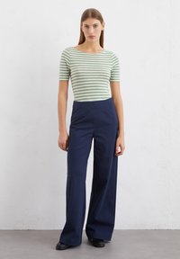 Gestreiftes grün-weißes, eng anliegendes Oberteil mit kurzen Ärmeln, kombiniert mit hoch taillierten, dunkelblauen weit geschnittenen Hosen, alles aus weichem Baumwollstoff gefertigt.