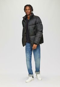 Zwarte gewatteerde jas met een hoge kraag, textuurafwerking, ritsluiting, gecombineerd met lichtblauwe jeans en witte sneakers.