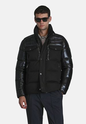 Black puffer jacket with glossy shoulders and matte body, features dual chest pockets, snap buttons, and a high collar. Worn with sunglasses.