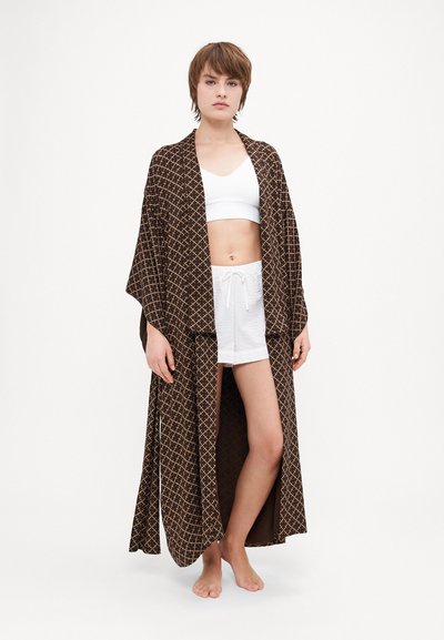 Kimono largo marrón con un patrón de cuadros, de tela ligera, con delantera abierta y mangas anchas, usado sobre una camiseta corta blanca y pantalones cortos.