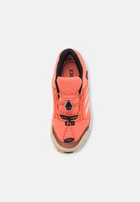 Zapato de senderismo rojo con parte superior de malla, acentos negros, cordones elásticos y suela de goma. Presenta una superficie texturizada y una puntera brillante.