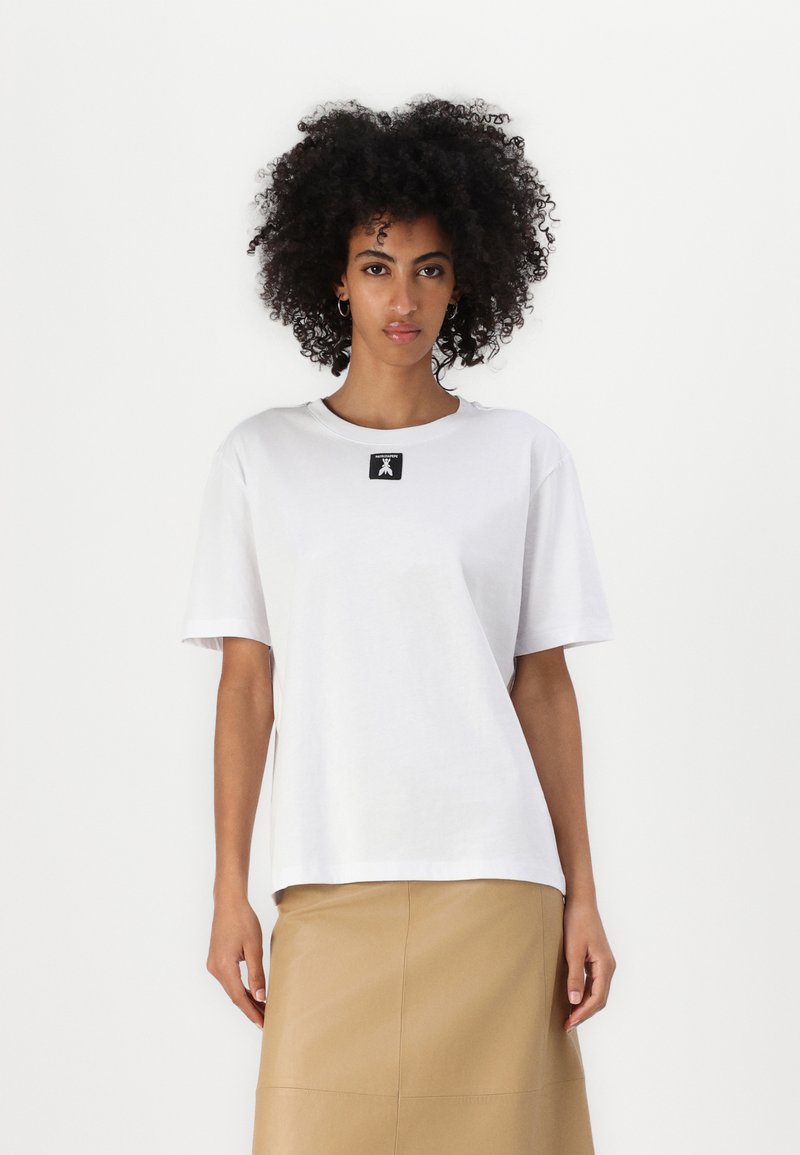 Balts kokvilnas T-krekls ar īsām piedurknēm, apaļu kakla izgriezumu un melnu logo plāksteri uz krūšu; gluda tekstūra un brīvs piegriezums.