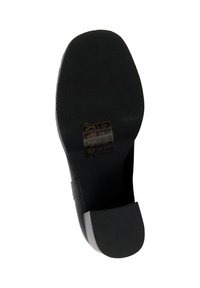 Semelle de chaussure noire avec une surface texturée, une forme arrondie et un léger talon. Présente un détail de logo avec des instructions d'entretien près du centre.