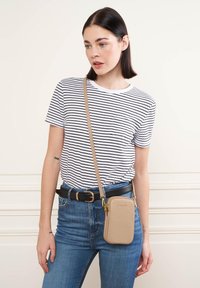 Borsa crossbody crema con finitura texturizzata, zip dorata e tracolla regolabile, indossata sopra una maglietta a righe blu e bianche e jeans di denim.