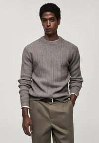 Gray ribbed knit sweater with a round neckline, long sleeves, and textured pattern; paired with beige trousers and a black belt.