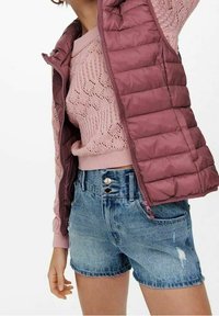 Lekka pikowana kamizelka w kolorze bordowym, zestawiona z różowym dzianinowym sweterkiem oraz postrzępionymi szortami dżinsowymi z detalami w postaci guzików i wykończeniem z frędzlami.