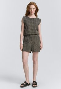 Completo in tessuto a righe composto da un top senza maniche con bordi arricciati e pantaloni corti, entrambi in bianco e nero. Indossato con sandali neri.