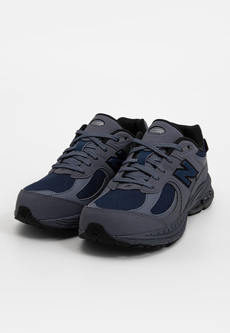 Graue Sportschuhe aus Mesh und synthetischem Material, mit abgerundeter Zehenkappe, gepolstertem Kragen und Schnürverschluss. Logo-Akzente in Marineblau.