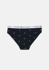 Tumesinised puuvillased püksikud valge TOMMY HILFIGER vöökohaga. Kangal on väikesed valged ristkülikukujulised logod, mis korduvad üle kogu pinna.