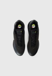 Black athletic shoes with a mesh upper, featuring a smooth texture, perforated pattern, and a rounded toe. "Air Max" branding visible.