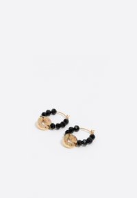 Pendientes de aro con cuentas facetadas negras y un acento circular en tono dorado con letras y diseños decorativos, creando texturas contrastantes.