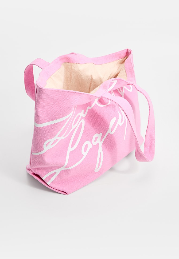 Sac fourre-tout en toile rose avec du texte en cursive blanc, intérieur beige et deux longues anses, présenté ouvert et vide sur un fond blanc.
