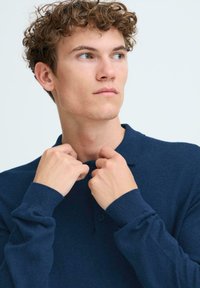 Polo de color azul marino con mangas largas y un cuello, que presenta una botonadura de dos botones y una suave tela de punto texturizada.