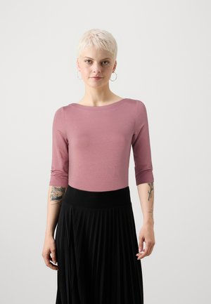 Tett, topp med trekvartermet i dempet rosa, laget av myk stoff. Kombinert med et svart plissert skjørt med bred midje.