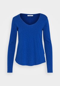 Pitkähihainen sininen T-paita, joka on valmistettu pehmeästä kankaasta ja jossa on V-pääntie, kaareva helma ja saumattomat hihansuut. Ihanteellinen arkikäyttöön.