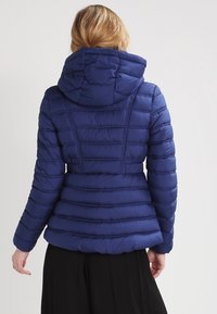 Tmavě modrá péřová bunda s kapucí, prošívaným designem a horizontálními švy. Materiál je hladký a vycpaný pro izolaci.