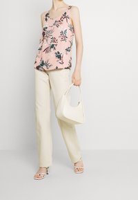 Top floreale rosa con motivi verdi e rossi, abbinato a pantaloni a gamba larga color crema e sandali con tacco bianchi e alla schiena. Porta una borsa bianca.