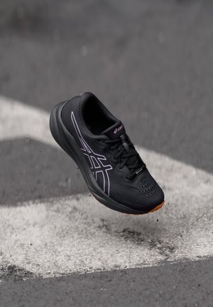 Black athletic shoe with a mesh upper, purple accents, textured surface, and a rubber sole. Features laces and streamlined shape.