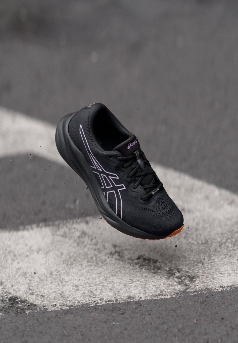 Baskets de sport noires avec tige en mesh, accents violets, surface texturée et semelle en caoutchouc. Comprend des lacets et une forme épurée.