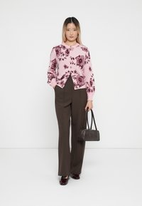 Rosa blomstermønstret cardigan med rund hals, sammen med brune højtaljede bukser og en lille mørk håndtaske. Glatte teksturer.