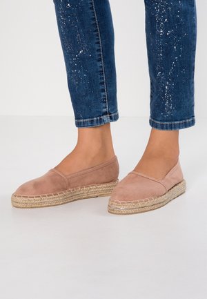 Voeten met lichtroze suède espadrilles gecombineerd met blauwe spijkerbroeken met witte verfspatten.