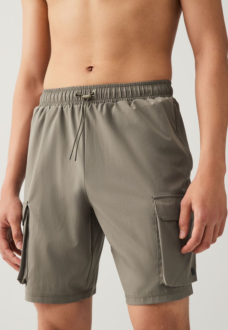 Shorts cargo en vert olive discret, avec une ceinture élastique, un cordon de serrage et des poches latérales pour le rangement. Tissu lisse et léger.