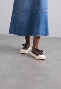 Bruine canvas sneakers met witte rubberen zolen, voorzien van bruine veters en oogjes. Gecombineerd met een lange spijkerrok.