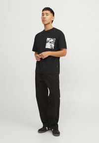 Sort t-shirt med en hvid blomsterprint lomme på venstre side; parret med sorte bukser og mørke sko; minimalistisk design.