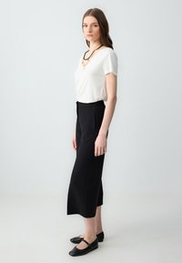 Haut blanc à manches courtes, pantalon noir taille haute, ballerines noires à lanière. Design simple, texture lisse et couleurs neutres.