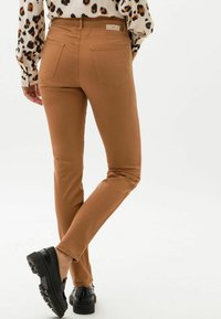 Vaqueros skinny marrones con una textura suave, que presentan dos bolsillos traseros y una etiqueta en la cintura, combinados con zapatos de plataforma negros.