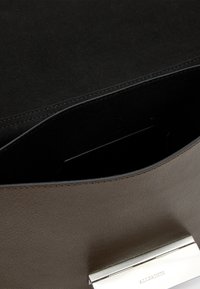 Brązowa skórzana torebka o miękkiej fakturze, z metalowym zapięciem w kolorze srebrnym i gładką, czarną podszewką wewnętrzną.