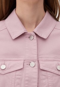 Chaqueta de mezclilla rosa clara con cuello, botones a presión plateados y bolsillos de solapa en el pecho. La tela tiene una textura suave.