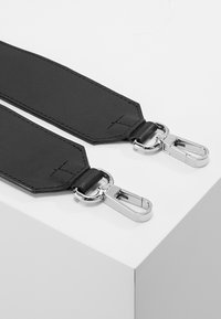 Bracelet en cuir noir avec des fermoirs en métal argenté, présentant une texture lisse et une forme plate, souligné par des détails de surpiqûre.