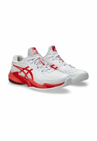 Des chaussures de sport blanches avec des accents rouges, présentant une tige texturée, des panneaux en mesh et une semelle en caoutchouc avec un motif de tread unique.