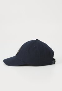 Casquette en coton bleu marine avec une visière incurvée, accent en métal au logo à l'avant, et une sangle ajustable à l'arrière. Texture lisse.