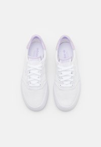 Bílé plátěné tenisky s levandulovými akcenty, kulatou špičkou, plochými tkaničkami a strukturovanou podrážkou. Logo Adidas na jazyku a boku.