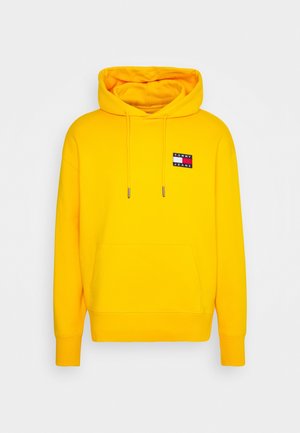 Knallig gelber Kapuzenpullover mit Fronttasche und Kordeln, mit einem kleinen rechteckigen "Tommy Jeans"-Logo auf der Brust.
