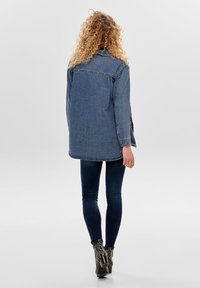 Denimjack met een relaxte pasvorm, lange mouwen en achterzakken. Donkerblauwe kleur met een licht rafelige zoom en knoopdetails.