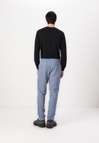 Svart långärmad skjorta i kombination med blå mönstrade byxor med vita sidostråk och en avslappnad passform, kompletterat med mörka skor.