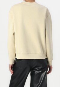 Felpa beige con colletto a coste, spalle scese e vestibilità rilassata. Indossata con pantaloni in pelle sintetica nera.