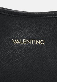 Sac en cuir noir avec une surface texturée. Comprend un logo doré "Valentino" bien en vue à l'avant.