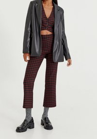 Zwarte nepleer blazer over een rood en zwart geblokt cropped top en bijpassende broek. Robuuste zwarte loafers en grijze sokken maken de look compleet.