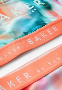 Farverigt badetøj med et flerfarvet, abstrakt mønster i blå og koral; har en koralstribe med hvid tekst "BAKER by TED BAKER."
