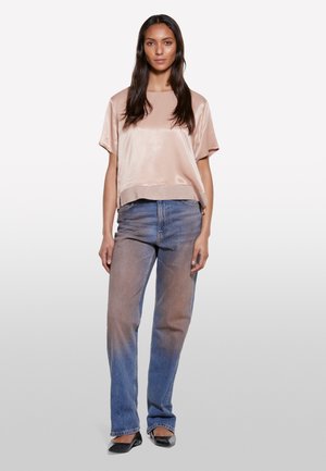 Haut en satin rose avec des manches courtes, coupe décontractée, associé à un jean droit délavé. Des ballerines noires complètent la tenue.