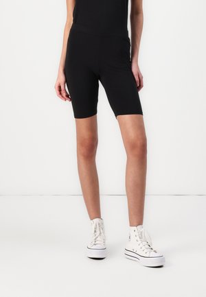 Black bicycle shorts made of stretchy fabric, featuring a high waistband. Worn with white high-top sneakers and a fitted black top.