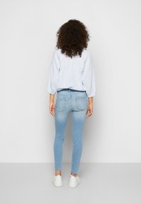 Jeans skinny de ganga azul claro com bolsos traseiros, combinados com uma blusa larga às riscas em azul claro e ténis brancos.
