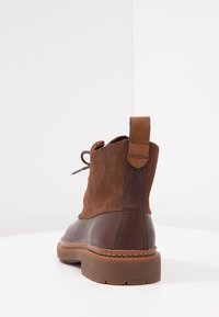 Botas de tobillo de cuero marrón y ante con acabado texturizado, punta redondeada, acentos cosidos y una lengüeta en el talón.